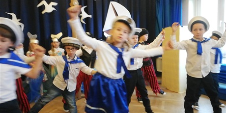 Powiększ grafikę: Na zdjęciu grupa dzieci w strojach biało niebieskich marynarskich z czapkami na głowach  podczas przedstawienia z okazji 45 lecia przedszkola.