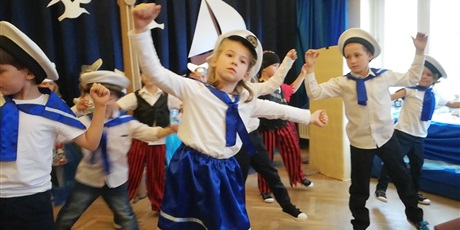Powiększ grafikę: Na zdjęciu grupa dzieci w strojach biało niebieskich marynarskich z czapkami na głowach  podczas przedstawienia z okazji 45 lecia przedszkola.