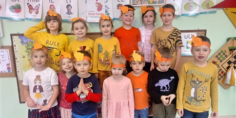 Powiększ grafikę: Na zdjęciu stoi grupa dzieci, przeważnie w strojach pomarańczowych i żółtych. Na głowach mają pomarańczowe papierowe opaski z pomarańczowymi słoniami.
