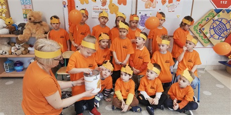 Powiększ grafikę: Zdjęcia przedtawia dzieci w sali przedszkolnej ubrane w pomarańczowe koszulki ,na głowach dzieci mają pomarańczowe opaski ze słoniem pomarańczowym