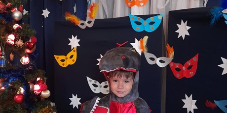 Powiększ grafikę: Na zdjęciu dziecko w wieku przedszkolnym w karnawałowym przebraniu. w tle kolorowe maski karnawałowe w kształcie kocich oczu oraz choinka .