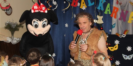 Powiększ grafikę: Na zdjęciu dzieci w wieku przedszkolnym w karnawałowym przebraniu podczas imprezy karnawałowej oraz Myszka Miki oraz mężczyzna z mikrofonem.