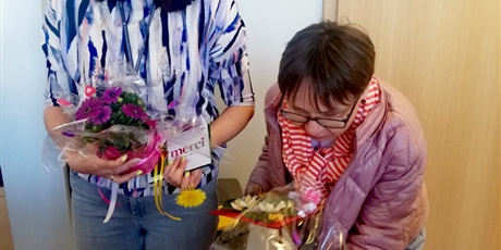 Powiększ grafikę: Na zdjęciu dwie kobiety z kolorowymi kwiatkami oraz życzniami w dłoni.