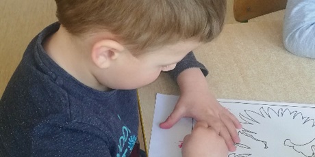 Powiększ grafikę: Na zdjęciu dziecko w wieku przedszkolnym kolorujące orała białego na czerwonym tle.