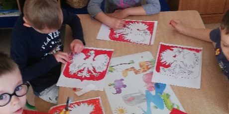Powiększ grafikę: Na zdjęciu dzieci w wieku przedszkolnym kolorujące orała białego na czerwonym tle.