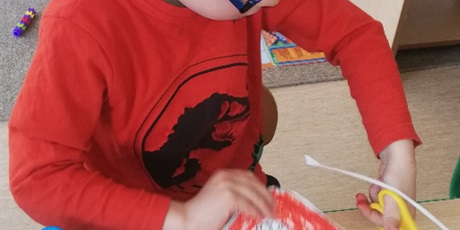 Powiększ grafikę: Na zdjęciu dziecko w wieku przedszkolnym kolorujące orała białego na czerwonym tle.