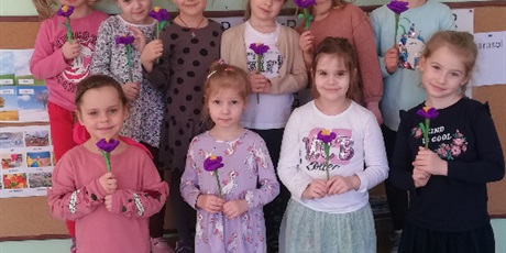 Powiększ grafikę: Na zdjęciu uśmiechnięte dziewczynki w ieku przedszkolnym z kwiatkami w dłoniach obchodzących dzień kobiet