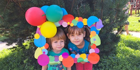 Powiększ grafikę: Na zdjęciu dzieci w wieku przedszkolnym na tle kolorowej ramki ozdobionej papierowymi kropkami i balonami.