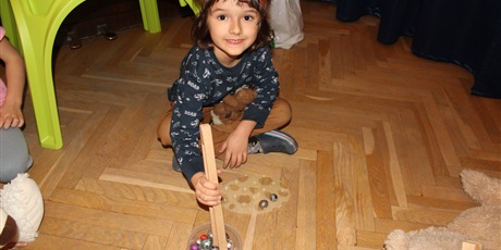 Powiększ grafikę: Na zdjęciu dziecko w wieku przedszkolnym układające szklane kolorowe kulki drewnianymi szczypcami.