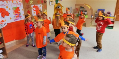 Powiększ grafikę: Na zdjęciu grupa dzieci ubranych  w koszulki koloru pomarańczowego podczas tańca.