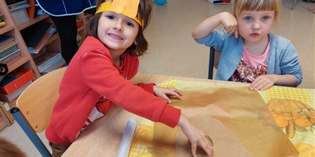 Powiększ grafikę: Na zdjęciu dzieci w pomarańczowych koszulkach w sali przedszkolnejj podczas wypieku ciasteczek
