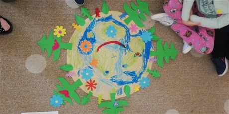Powiększ grafikę: Plakat papierowy ziemi z zielonymi choinkami ,niebieskimi kwiatkami i luddzikmi wykonany przez dzieci w wieku przedszkolnym.