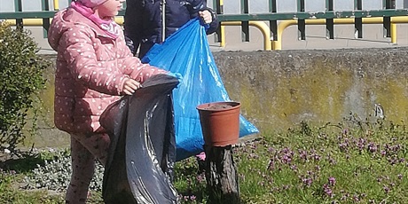 Powiększ grafikę: Na zdjęciu grupa dzieci w wieku przedszkolnym z workami na śmieci sprzatająca teren przedszkola