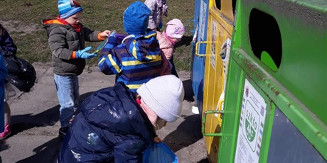 Powiększ grafikę: Na zdjęciu grupa dzieci w wieku przedszkolnym z workami na śmieci sprzatająca teren przedszkola