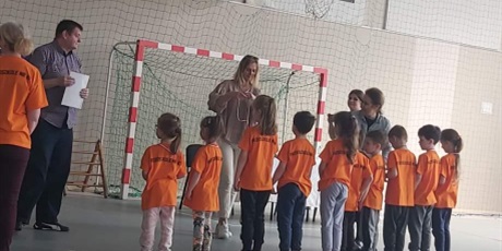 Powiększ grafikę: Na zdjęciu grupa dzieci w wieku przedszkolnym w pomarańczowych koszulkach.