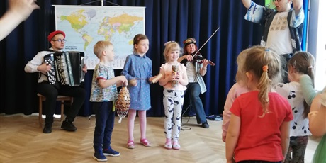 Powiększ grafikę: Na zdjęciu grupa dzieci w wieku przedszkolnym na sali gimnastycznej pdczas  próby grania na instrumentach muzycznych oraz muzycy.
