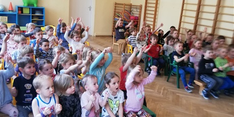 Powiększ grafikę: Na zdjęciu grupa dzieci w wieku przedszkolnym na sali gimnastycznej pdczas  oglądania muzycznego