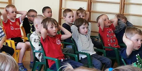 Powiększ grafikę: Na zdjęciu grupa dzieci w wieku przedszkolnym na sali gimnastycznej pdczas  oglądania muzycznego.