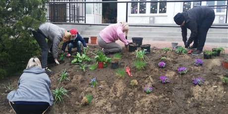 Powiększ grafikę: Na zdjęciu grupa ludzi dorosłych  sadząca kwiaty wiosenne w ziemi na górce