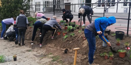 Powiększ grafikę: Na zdjęciu grupa ludzi sadząca kwiaty wiosenne w ziemi na górce.