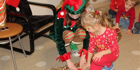 Powiększ grafikę: Na zdjęciu dziewczynka w czerwonym ubraniu z Elfem rozwiązują zagdkę mikołajkową