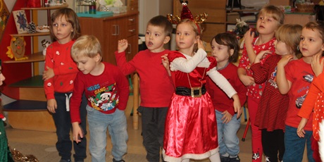 Powiększ grafikę: Na zdjeciu grupa dzieci w wieku przedszkolnych w subraniach koloru czerwonego bawią sie do muzyki mikołajkowej