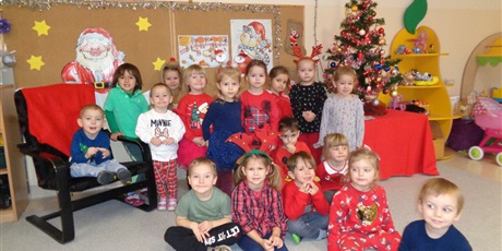 Powiększ grafikę: Na zdjęciu grupa dzieci w wieku przedszkolnym ubranych kolorowo.w tle choinka  i dekoracja mikołajkowa