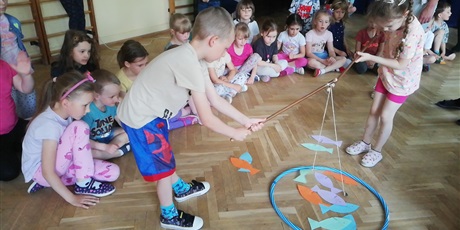 Powiększ grafikę: Na zdjęciu dzieci w wieku przedszkolnym  łowiące kolorowe papierowe rybki z drewnianej podłogi
