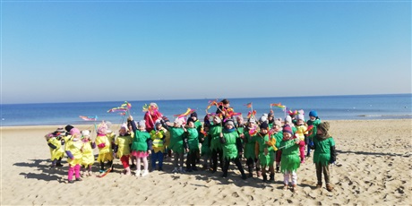 Powiększ grafikę: Na zdjęciu dzieci w kolorowych strojach z panią wiosną na plaży.
