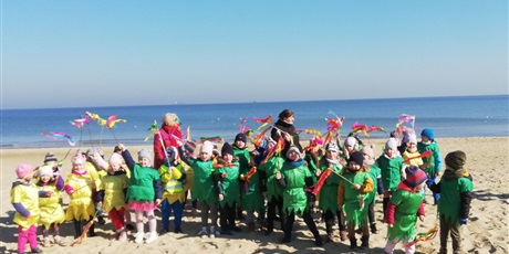 Powiększ grafikę: Na zdjęciu dzieci w kolorowych strojach z panią wiosną na plaży.