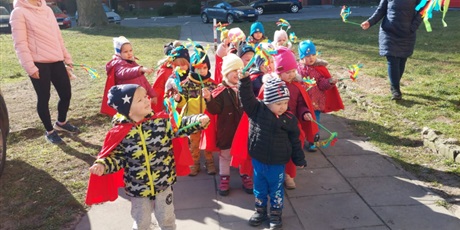 Powiększ grafikę: Na zdjęciu dzieci maszerujący ulicą w kolorowych strojach, śpiewające piosenki o wiośnie i witające wiosnę.