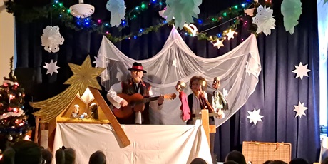 Powiększ grafikę: Na zdjęciu aktor z gitarą  i aktorka z pacynkami w tle szopka bożonarodzeniowa.