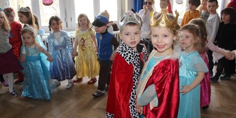 Powiększ grafikę: Na zdjęciu grupa dzieci w strojach karnawałowych podczas zabaw z okazji tłustego czwartku oraz król i królowa pączków.