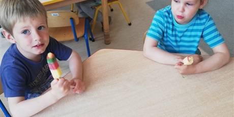 Powiększ grafikę: Na zdjeciu grupa dzieci w wielu przedszkolnym siedząca przy stoliku i jedząca kolorowe lody