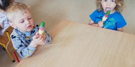 Powiększ grafikę: Na zdjeciu grupa dzieci w wielu przedszkolnym siedząca przy stoliku i jedząca kolorowe lody