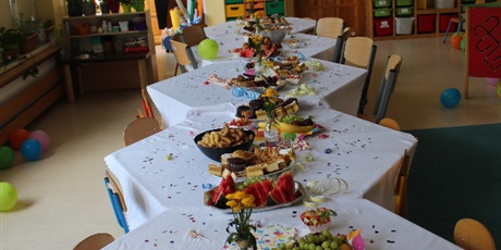 Powiększ grafikę: Na zdjęciu stoliki w sali przedszkolnej z talerzykami z  ciastkami i owocami.