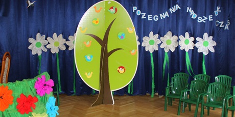 Powiększ grafikę: Na zdjęciu kolorowa dekoracja kwiaty z bibibuły ,drzewo zielone plastikowe krzesełka