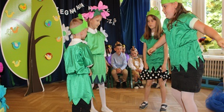 Powiększ grafikę: Na zdjęciu dzieci w wieku przedszkolnym w kolorowych strojach żabek i kwiatka  podczas przedstawienia z okazji zakończenia roku przedszkolnego