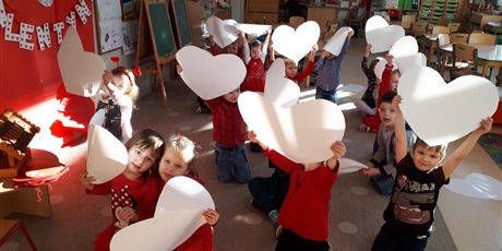 Powiększ grafikę: Na zdjęciu dzieci podczas zabaw walentynkowych z białymi sercami papierowymi w dłoniach.