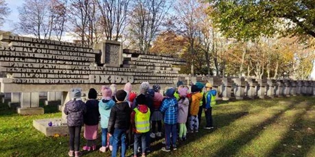 Powiększ grafikę: Na zdjęciu grupa dzieci  w wieku przedszkolnym przed pomnikiem na cmentarzu.