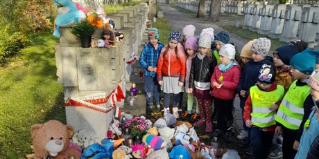 Powiększ grafikę: Na zdjęciu grupa dzieci  w wieku przedszkolnym przed pomnikiem na cmentarzu.