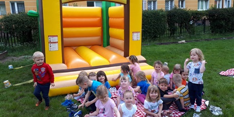 Powiększ grafikę: Na zdjęciu rupa dzieci w wieku przedszkolnym i żółta dmuchana zabawka na trawie do skakania.