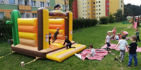 Powiększ grafikę: Na zdjęciu dmuchany zamek na trawie i bawiące się wokół dzieci w wieku przedszkolnym.