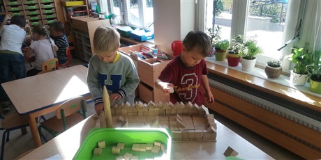 Powiększ grafikę: Na zdjęciu dzieci w sali przedszkolnej budującez drewnianych klocków zamek