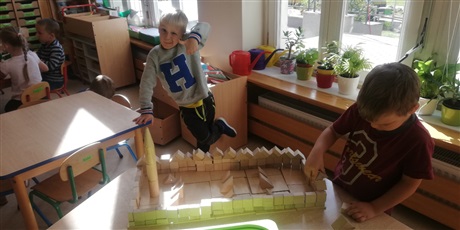 Powiększ grafikę: Na zdjęciu dzieci w sali przedszkolnej budującez drewnianych klocków zamek.