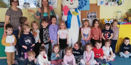 Powiększ grafikę: Na zdjęciu dzieci w wieu kprzedszkolnym w sali przedszkolnej i pluszowy zając z panią Wiosną