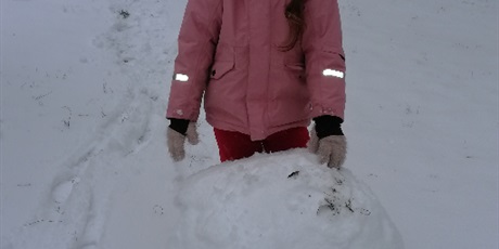 Powiększ grafikę: Dziewczynka poczas zabaw na śniegu na przedszkolnym placu zabaw toczaca kulę śnieżną