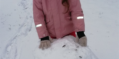 Powiększ grafikę: Dziewczynka poczas zabaw na śniegu na przedszkolnym placu zabaw toczaca kulę śnieżną
