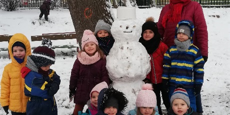 Powiększ grafikę: Zimowe zdjęcie dzieci i pani na przedszkolnym placu zabaw z bałwankiem