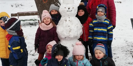 Powiększ grafikę: Zimowe zdjęcie dzieci i pani na przedszkolnym placu zabaw z bałwankiem
